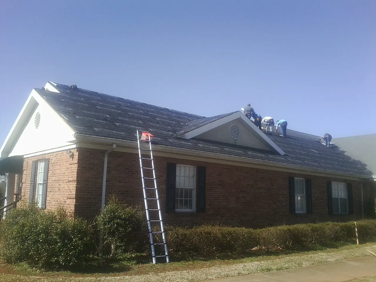 Crew tearing shingles off a brick ranch roof with a ladder set — Metal Roof Repair work by our crew in Mc Adenville