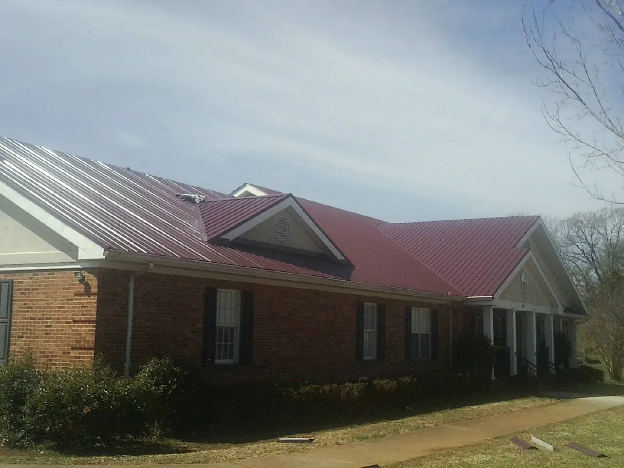 Red metal roof with gabled entries on a long brick building, from a Hail Damage Roof Repair job in Mc Adenville