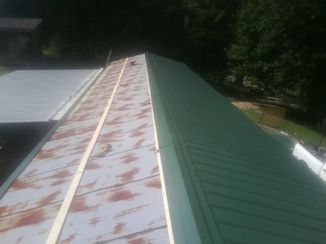 Old rusted panels beside newly installed green metal roofing — Wind Damage Roof Repair by Roofing Brothers in Mc Adenville