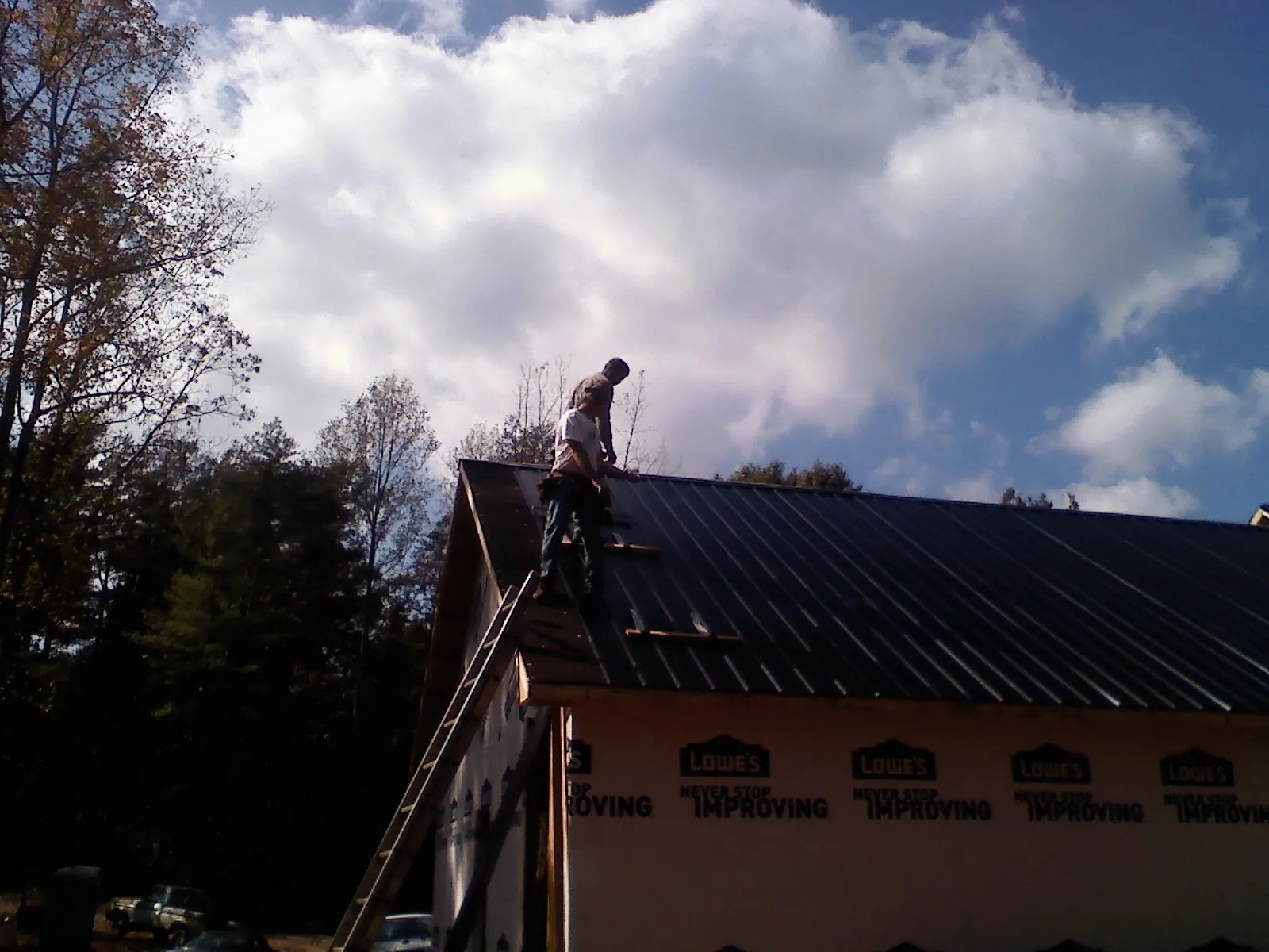 Roofer fastening dark metal panels high against a cloudy sky, from a Roof Inspection job in Mc Adenville