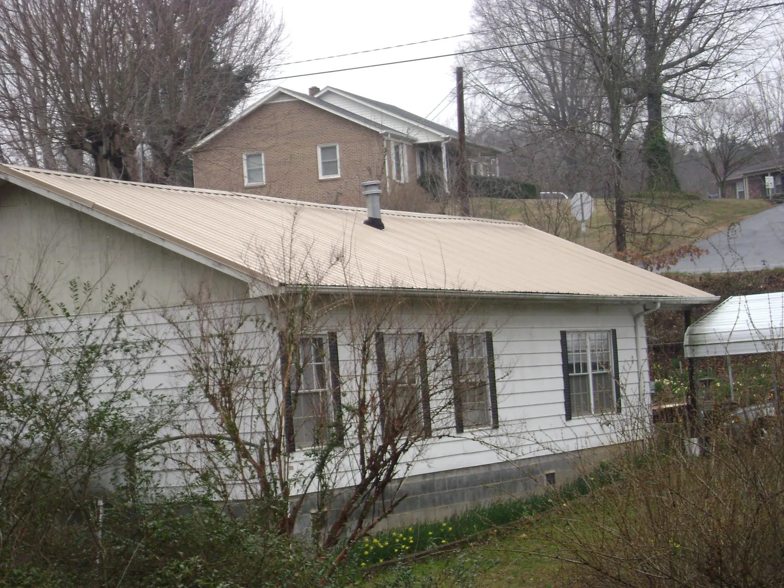 Tan metal roof on a white sided house set into a hillside — Commercial Roofing by Roofing Brothers in Mc Adenville